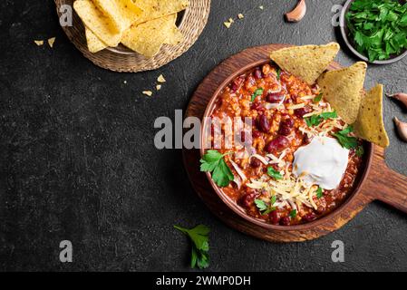 Chili con carne with cheese topings and nachos on black background, top view, copy space. Traditional mexican food, chili with red beans and ground be Stock Photo