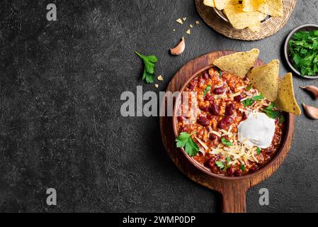 Chili con carne with cheese topings and nachos on black background, top view, copy space. Traditional mexican food, chili with red beans and ground be Stock Photo
