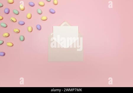 Top view of colourful easter eggs, pink envelope, white card on pink background. Creative easter composition, spring, copy space, flat lay. Stock Photo