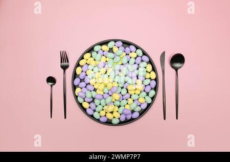 Top view of colourful easter eggs in black plate on pink background. Table setting, black plate and cutlery. Creative easter composition, spring. Stock Photo