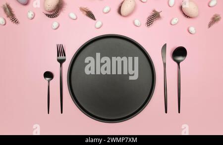 Top view of easter eggs, feathers, black plate and cutlery on pink background. Creative easter composition, spring, flat lay, copy space. Stock Photo