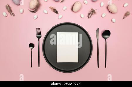 Top view of easter eggs, feathers, white card, black plate and cutlery on pink background. Creative easter composition, spring, flat lay, copy space. Stock Photo