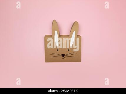 Top view of kraft bunny gift bag on pink background. Creative easter composition, spring, copy space, flat lay. Stock Photo