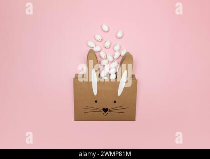 Top view of kraft bunny gift bag, white easter eggs on pink background. Creative easter composition, spring, copy space, flat lay. Stock Photo