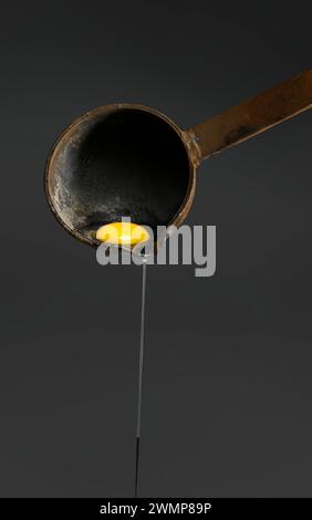 Close-up of egg-white being separated from the egg yolk and dripping out of an old, rusted ladle on a dark background; Studio Shot Stock Photo