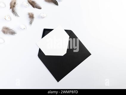 Top view of brown feathers, white easter eggs, black envelope and white card on white background. Creative easter composition, spring, copy space. Stock Photo