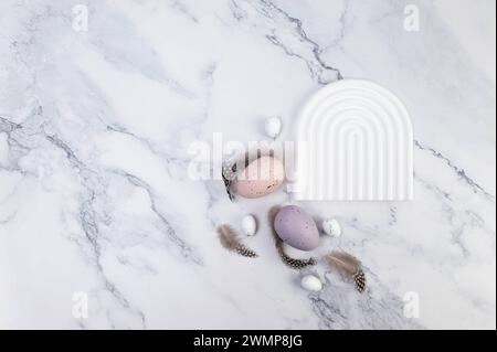 Top view of colourful easter eggs on white marble background. White arch tray, product presentation. Creative easter composition, spring, copy space. Stock Photo