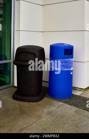 A black garbage can and a blue recycle can outside a building. Stock Photo