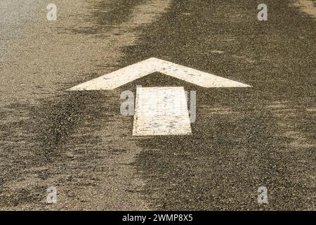 A white arrow sign painted on pavement indicting that the direction to be driven is straight. Stock Photo