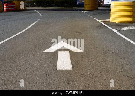 White arrow painted between two lines on the pavement at a ferry terminal indicating the direction of travel is straight. Stock Photo