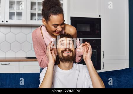 handsome man looking at his african american girlfriend after she surprised him and closed eyes Stock Photo
