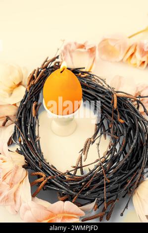 candle in the shape of an egg. Easter, holidays, traditions and object concept - burning candles in the shape of eggs and tulip flowers over a Stock Photo