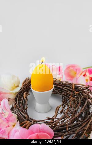 candle in the shape of an egg. Easter, holidays, traditions and object concept - burning candles in the shape of eggs and tulip flowers over a Stock Photo