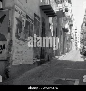 1970s, historical, side street, Via Mandralisca, Cefalu, Sicily, Italy.....fly posters on a wall for Molinari, an Italian liqueur, San Pellegrino water and one for jazz band Inconrtro '74, saying tickets are available from Piazza Umberto, the famous square located in the centre of Capri. A Fiat Punto parked up in the narrow cobbled street. Stock Photo