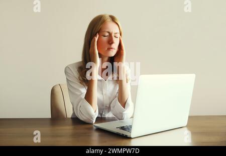 Tired overworked woman employee suffering from headache, migraine, working with laptop sitting at desk in office in morning Stock Photo