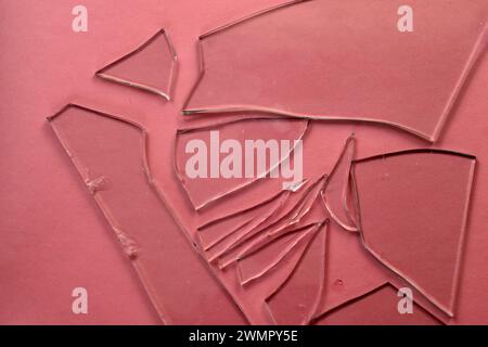Shards from broken glass of various shapes and sizes lie on a pink background. Stock Photo