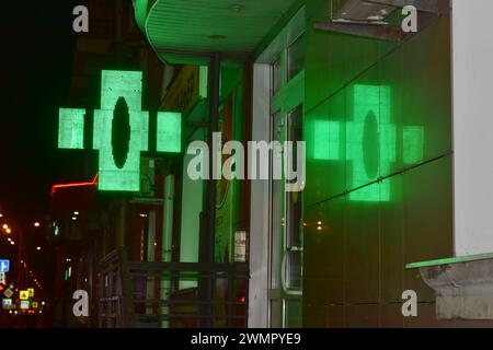 The picture shows the city at night. On the wall, lined with ceramic tiles, a pharmacy green cross is reflected. Stock Photo