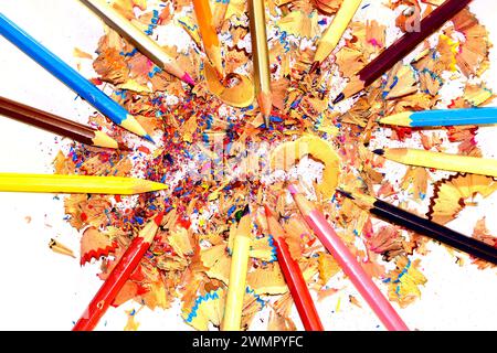 Colored pencils lie on wood shavings that lie on white. Stock Photo