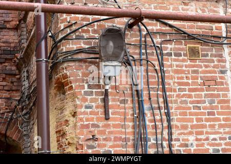 A forgotten idle lantern and several electrical wires hang on an old stone wall. Stock Photo