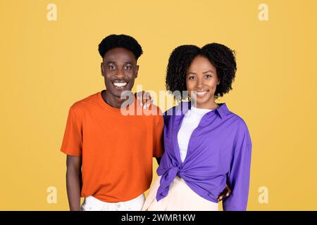 A smiling young woman in a purple blouse and a young man in an orange shirt standing shoulder to shoulder Stock Photo