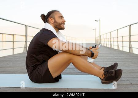 guy in sportswear uses smartphone for workout guidance sitting outdoors Stock Photo
