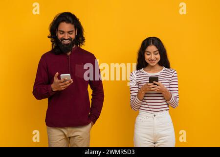 Millennial indian man and woman using cell phones on yellow Stock Photo