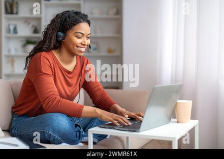 Smiling Young Black Woman Wearing Headset Using Laptop Computer At Home Stock Photo