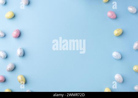 Festive Easter background. Multicoloured Easter eggs on a blue table. Card with a place for text. Top view. Stock Photo