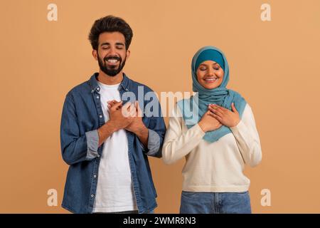 Thankful Muslim Couple Keeping Hands On Chest, Expressing Gratitude Together Stock Photo