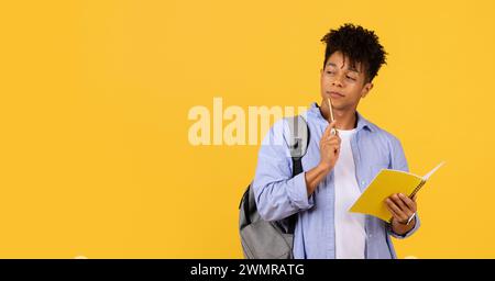 Thoughtful male student with notebook and pencil on yellow background Stock Photo