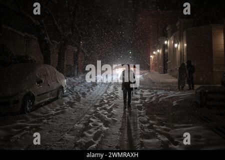 Teheran, Iran. 27th Feb, 2024. A woman with an umbrella walks along a street at night. The capital is snowed in after heavy snowfall. There is chaos on the streets and many people are abandoning their cars and walking home. Iran's national gas company has called on people to conserve energy due to possible shortages. Credit: Arne Bänsch/dpa/Alamy Live News Stock Photo