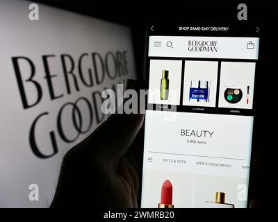 Person holding cellphone with webpage of US luxury department store company Bergdorf Goodman Inc. with logo. Focus on center of phone display. Stock Photo