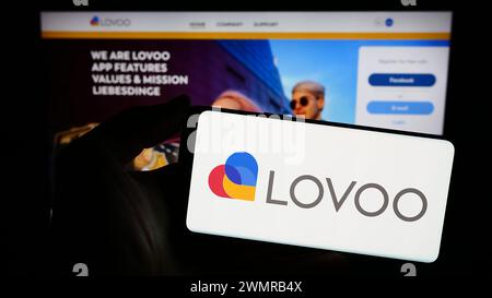 Person holding smartphone with logo of German online dating platform company LOVOO in front of website. Focus on phone display. Stock Photo