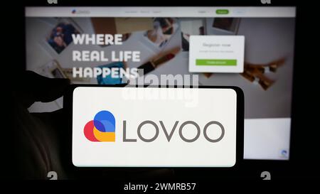 Person holding cellphone with logo of German online dating platform company LOVOO in front of business webpage. Focus on phone display. Stock Photo