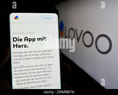 Person holding mobile phone with web page of German online dating platform company LOVOO in front of logo. Focus on center of phone display. Stock Photo
