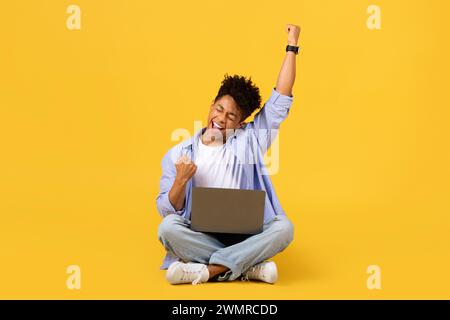 Exuberant black male student celebrating with laptop on yellow background Stock Photo