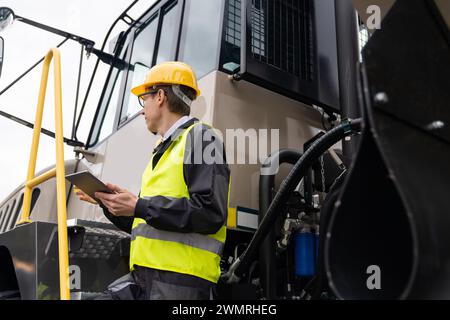 Engineer with tablet computer stands on the stairs to the cab of a truck. Stock Photo