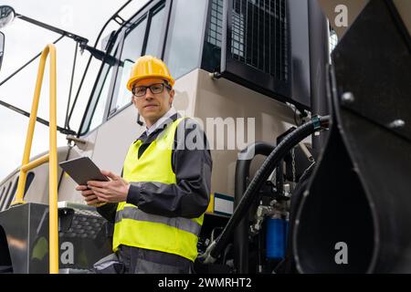 Engineer with tablet computer stands on the stairs to the cab of a truck. Stock Photo
