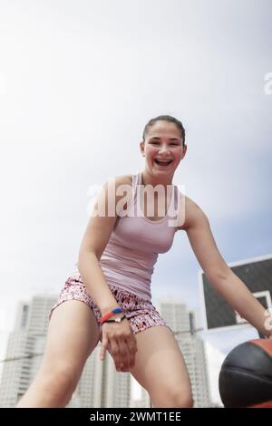 Girl playing basketball. Player bouncing ball. Outdoor sports field in urban surroundings. Stock Photo