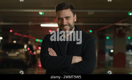 Portrait smiling Caucasian businessman boss adult man posing crossed arms pose in garage underground parking confident guy automobile seller driver of Stock Photo