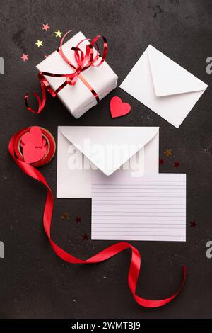 Envelopes with blank card, gift box and decor on black grunge background. Valentine's Day celebration Stock Photo