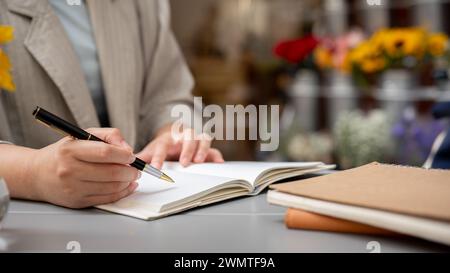 A cropped shot of a businesswoman or writer taking notes or writing something in her book while working remotely at a cafe. Stock Photo