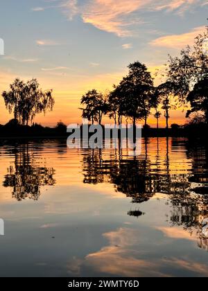 Sunset reflects in water with trees mirroring in tranquil scenery Stock Photo