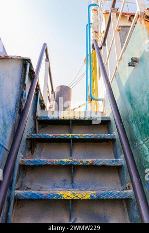 Old rusty vertical staircase with paint peeling off, leading to the upper deck of the wreck of cargo ship beached on the Al Hamriyah beach in UAE. Stock Photo