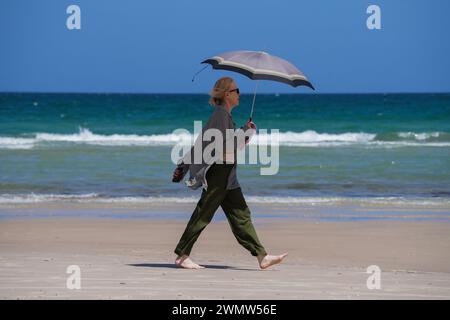 Adelaide, SA Australia 28 February 2024 .A woman shelters with an umbrella  from the hot sun while walking along the beach in Adelaide as temperatures reach 36celsius today  Credit: amer ghazzal/Alamy Live News Stock Photo