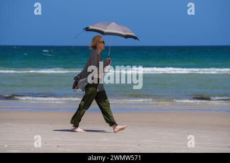 Adelaide, SA Australia 28 February 2024 .A woman shelters with an umbrella  from the hot sun while walking along the beach in Adelaide as temperatures reach 36celsius today  Credit: amer ghazzal/Alamy Live News Stock Photo