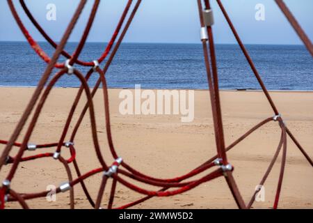 Red rope sections fastened with a metal clamp on a background of brown sand and blue sea Stock Photo