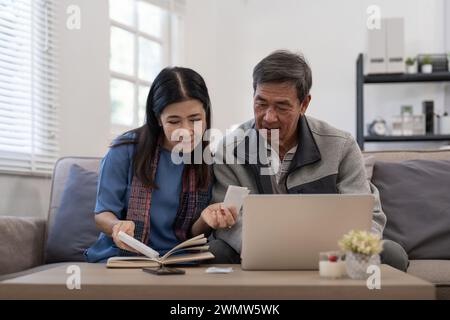 Asian senior couple checking and calculate financial bill together on sofa involved in financial paperwork, paying tax online using laptop at living Stock Photo