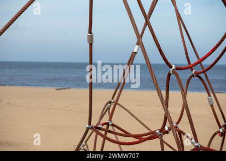 Red rope sections fastened with a metal clamp on a background of brown sand and blue sea Stock Photo