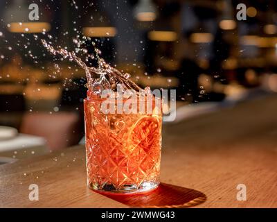 Orange or red drink with splash and droplets and orange slice garnish on bar counter. Red brown cocktail with splashes in pub or nightclub or restaurant Stock Photo